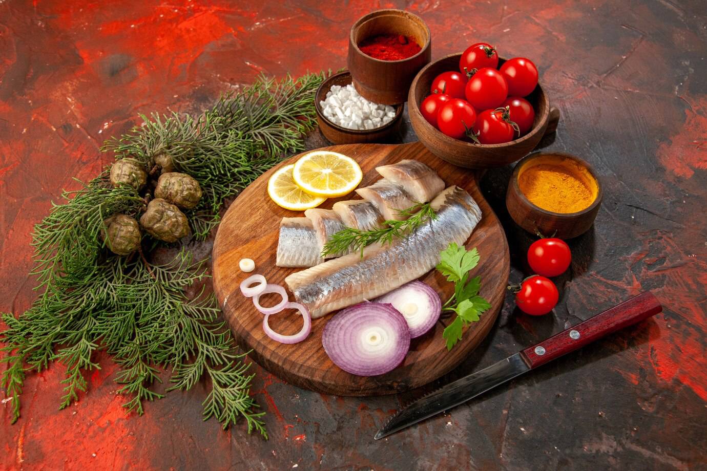A wooden cutting board features fresh fish fillets, lemon slices, red onions, herbs, cherry tomatoes, and spices, against a vibrant backdrop.