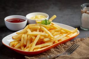 A plate of golden French fries garnished with parsley, accompanied by ketchup and mayonnaise in small bowls.
