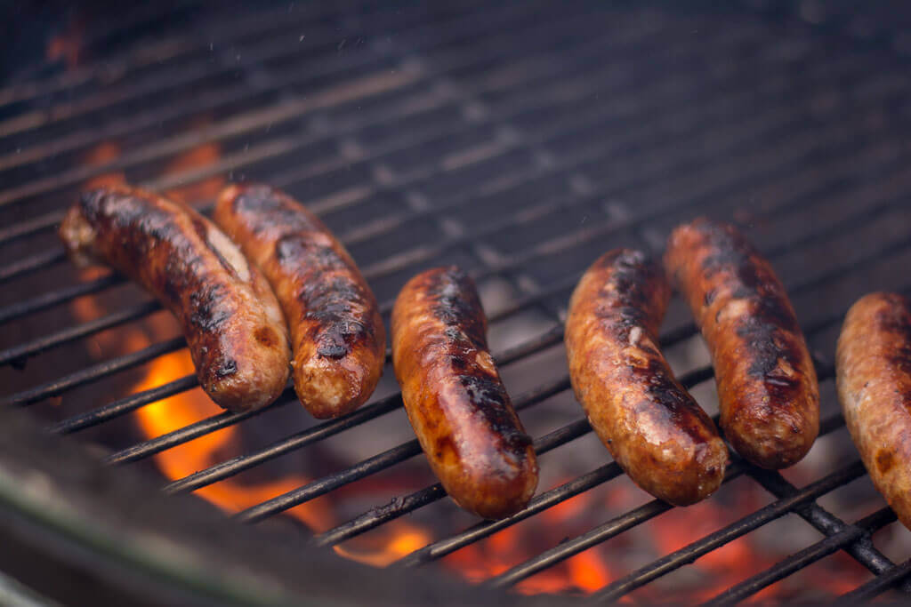 Grilled sausages sizzling on a barbecue grill, with smoky flames and a charred exterior, ready to be served.