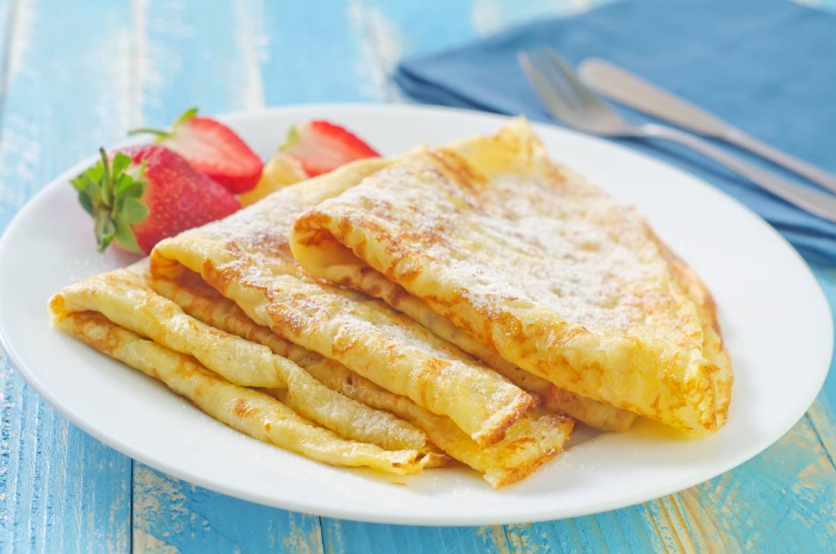 A plate of folded crepes dusted with powdered sugar, garnished with fresh strawberries, set on a light blue table.