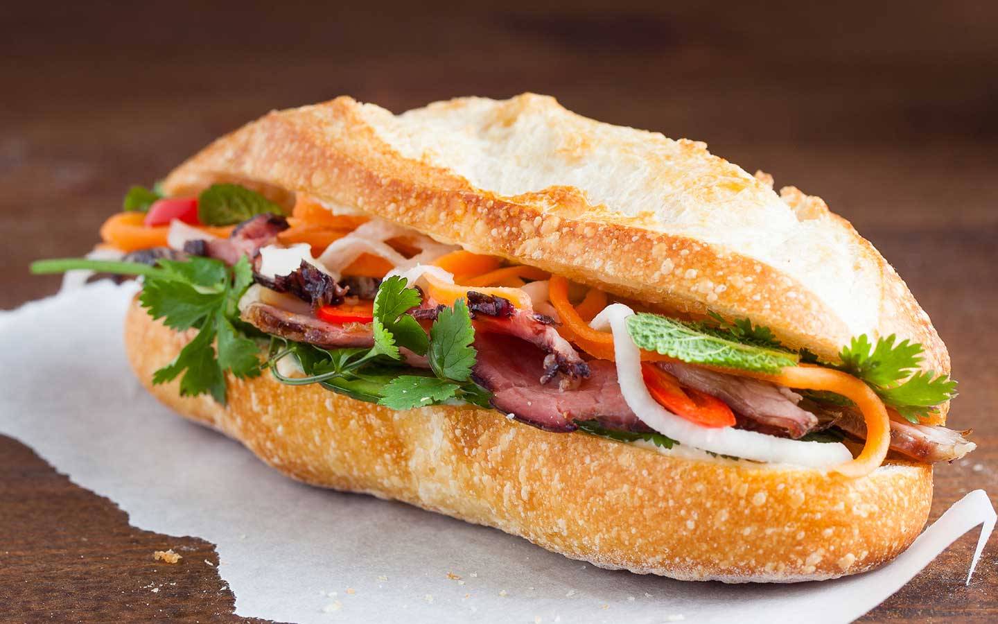 A delicious banh mi sandwich filled with roasted meat, fresh vegetables, herbs, and spicy toppings, served in a baguette.