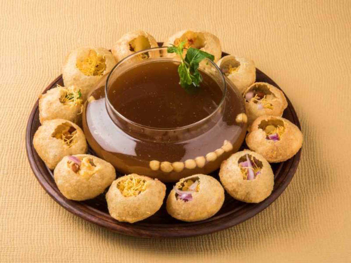 A platter of crispy puris filled with savory fillings, surrounded by a bowl of tangy tamarind water, garnished with mint.