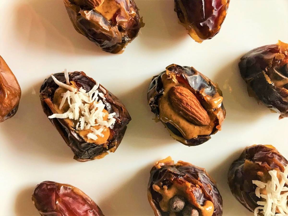 Stuffed dates topped with peanut butter, almonds, and coconut flakes on a white plate, showcasing a delicious snack.