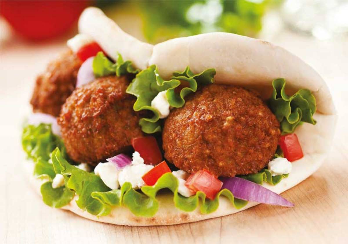 Close-up of a pita pocket filled with falafel balls, fresh lettuce, diced tomatoes, red onion, and creamy feta cheese.