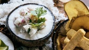 A coconut shell filled with ceviche, topped with cilantro, alongside crispy plantain chips and coconut shavings.