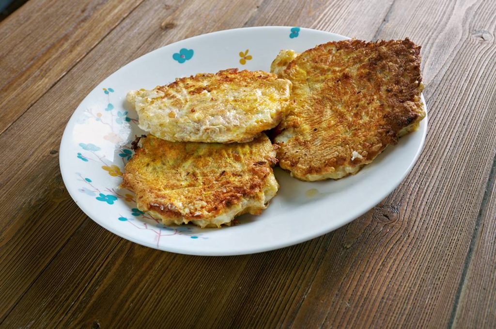 Four golden-brown, crispy pancakes on a white plate with floral accents, resting on a rustic wooden table.