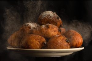 A plate of golden-brown, powder-sugar-dusted doughnuts with a light mist of flour, against a dark backdrop.
